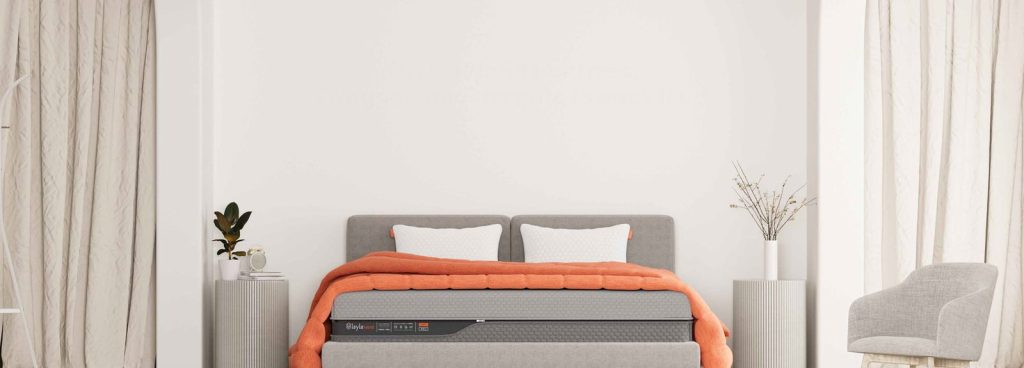 Layla Hybrid Mattress made up with orange bedding in a wide bedroom