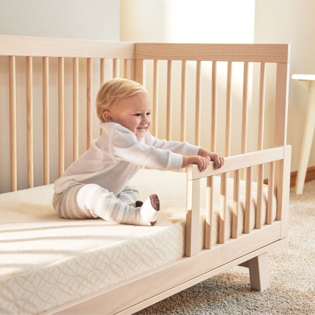 Toddler sitting on the Naturepedic Breathable Ultra in a convertible crib