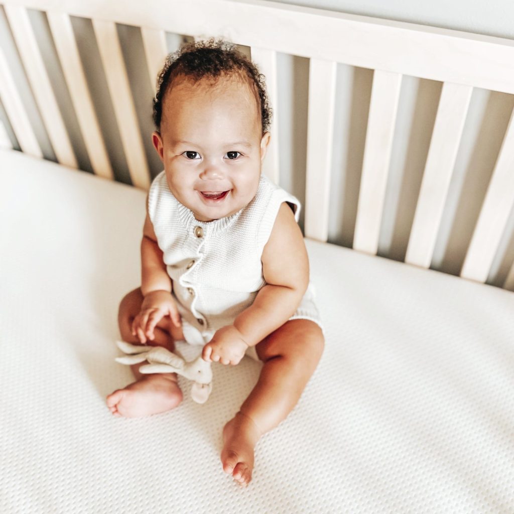 Toddler sitting on the Newton Essential crib mattress in a crib