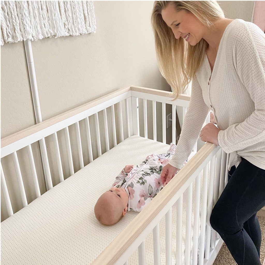 Mother leaning over a crib with a baby on the Newton Essential mattress