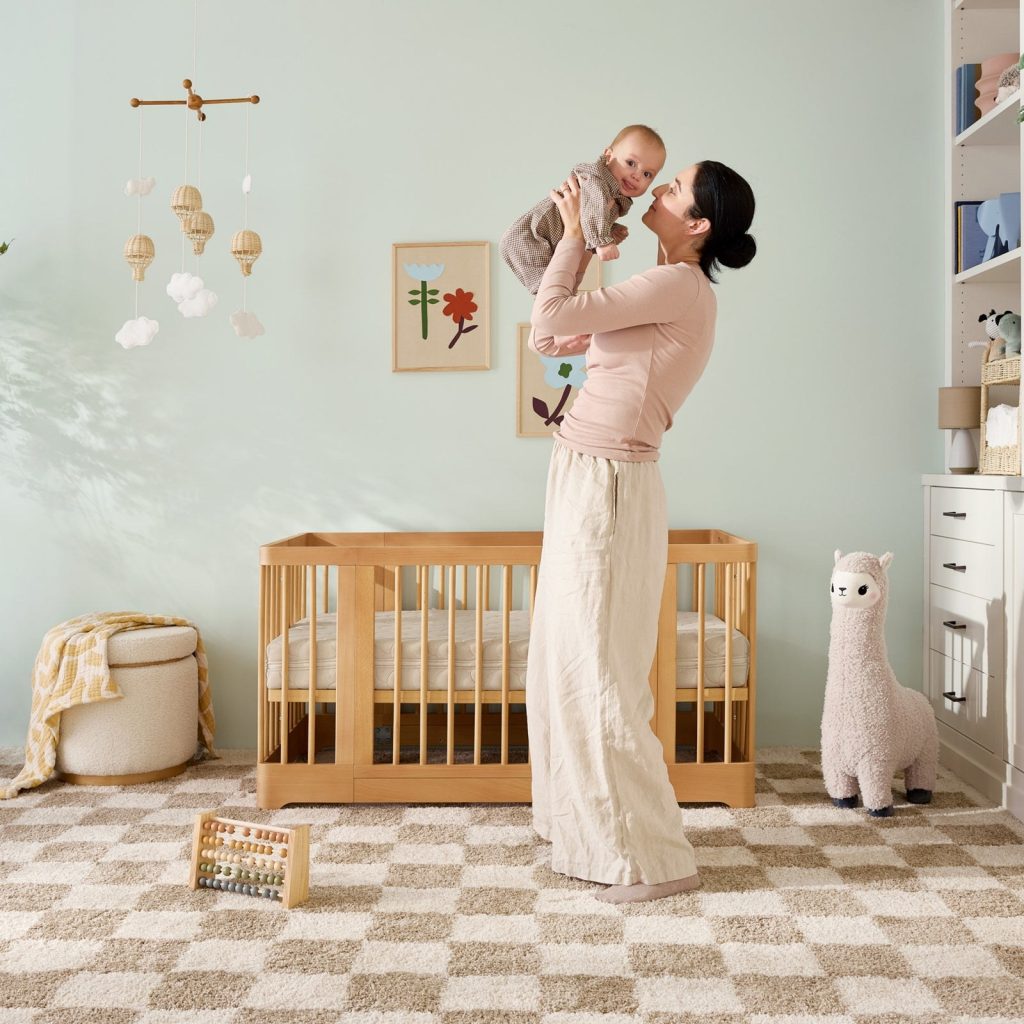 Parent holding a baby next to a crib with the Newton Original mattress in a nursery