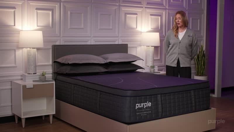 Purple staff member presenting a RejuvenatePlus mattress in a showroom bedroom
