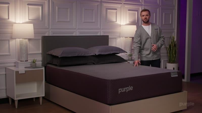 Purple staff member standing next to a RestorePremier Hybrid in a showroom bedroom
