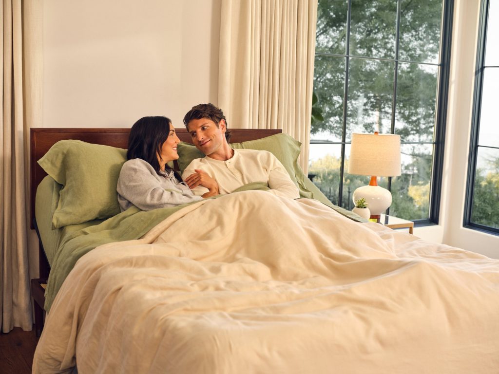 Couple talking in a made bed on a Purple Essential collection mattress