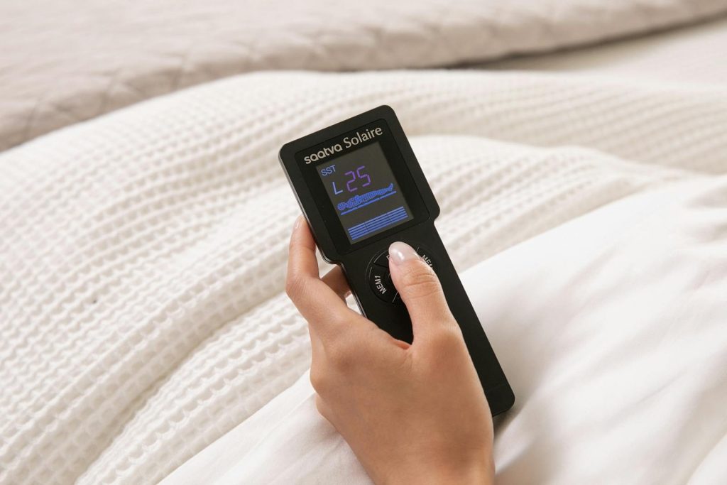Hand holding the Saatva Solaire remote over the pillow top