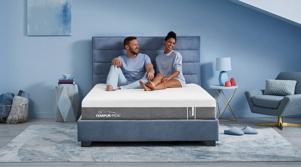 Couple sitting on a TEMPUR-Cloud mattress in a blue bedroom